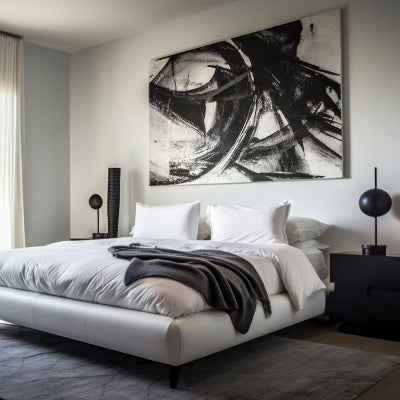 Modern minimalist bedroom with oversized black and white abstract artwork above a low white bed and large sunlit windows.