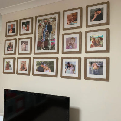 Gallery wall of framed family photos in matching wooden frames arranged in a neat grid on a beige wall